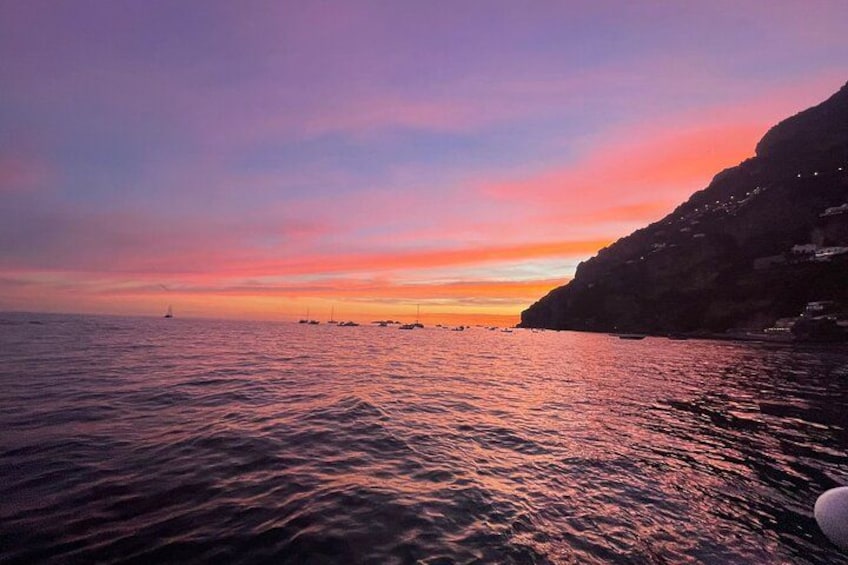 Un coucher de soleil sur une zone côtière, avec des bateaux et une falaise. 2