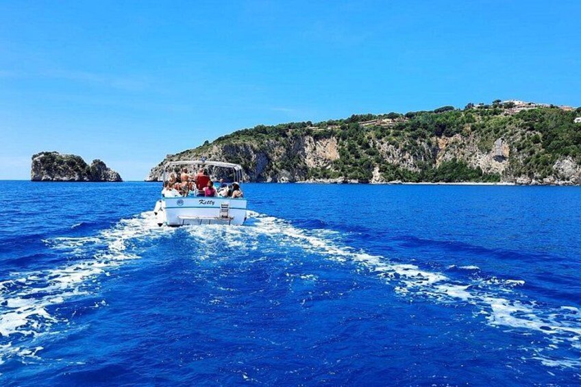 A boat with passengers on a clear blue sea, a rocky coastline, and a hill with vegetation. 4