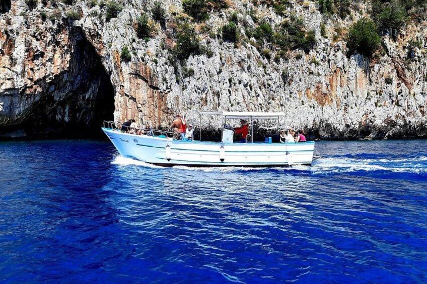 A boat on a blue sea with rocky cliffs in the background. 3