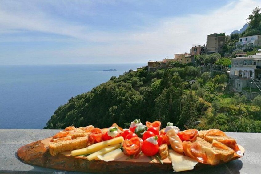 A wooden board with bread, tomatoes, and cheese against a coastal backdrop. 3