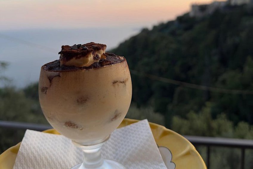 Un dessert servi dans un verre, posé sur une assiette jaune, avec un paysage pittoresque en arrière-plan. 3