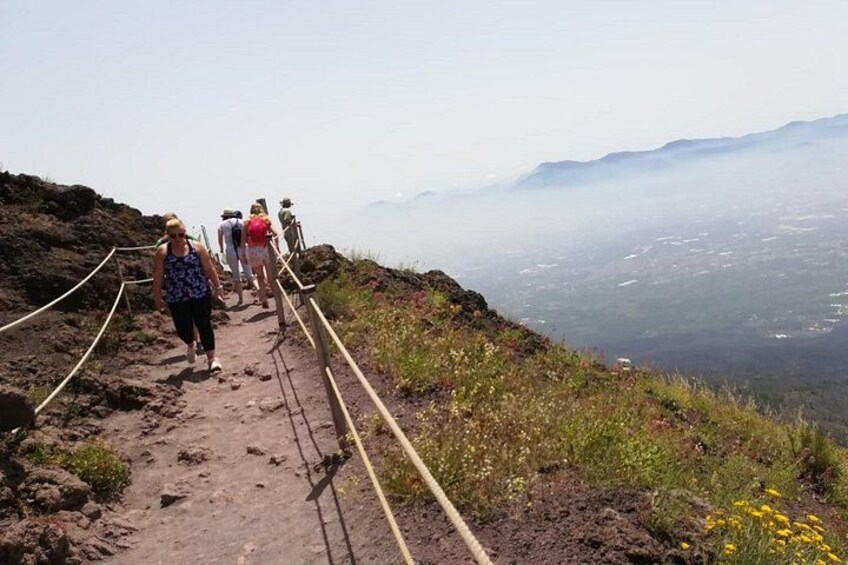 Un grupo de personas caminando por un sendero de tierra con barandillas en una ladera de montaña. 2