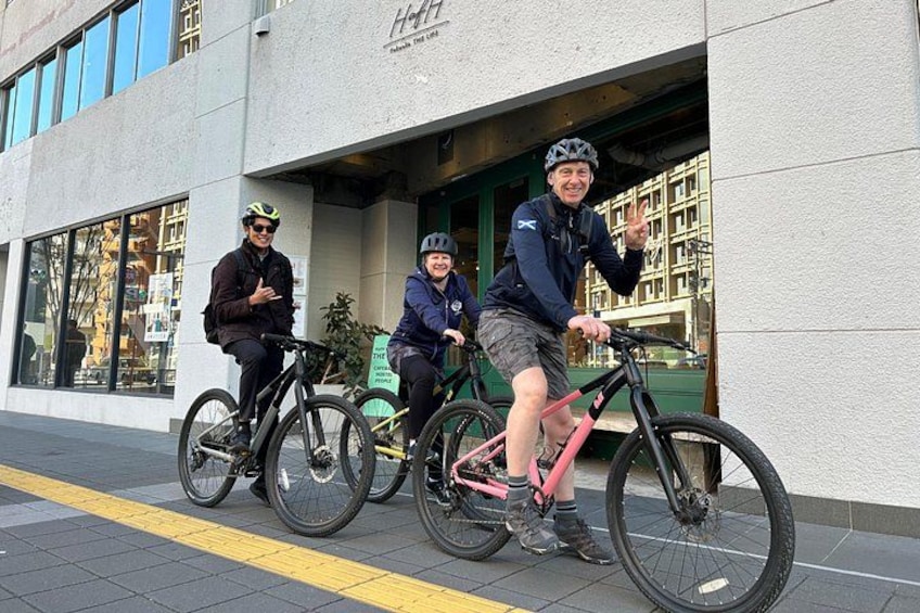 Tres personas en bicicletas frente a un edificio con grandes ventanales y un letrero. 2