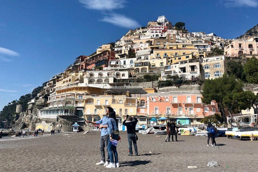 Una pittoresca cittadina costiera con edifici colorati su una collina, una spiaggia sabbiosa e persone che passeggiano. 1