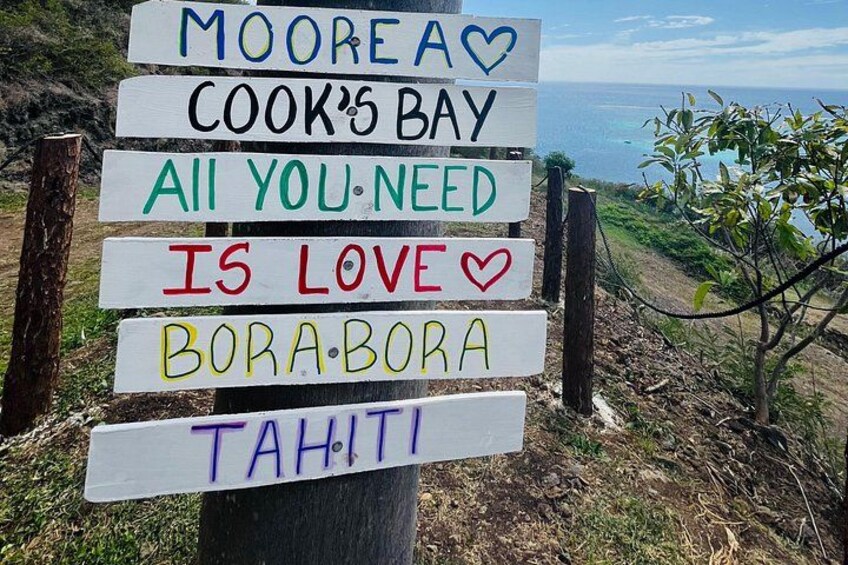 Een bord met verschillende teksten, waaronder 'MOORE A', 'COOK'S BAY', 'ALL YOU NEED IS LOVE', 'BORA.BORA' en 'TAHITI'. 2