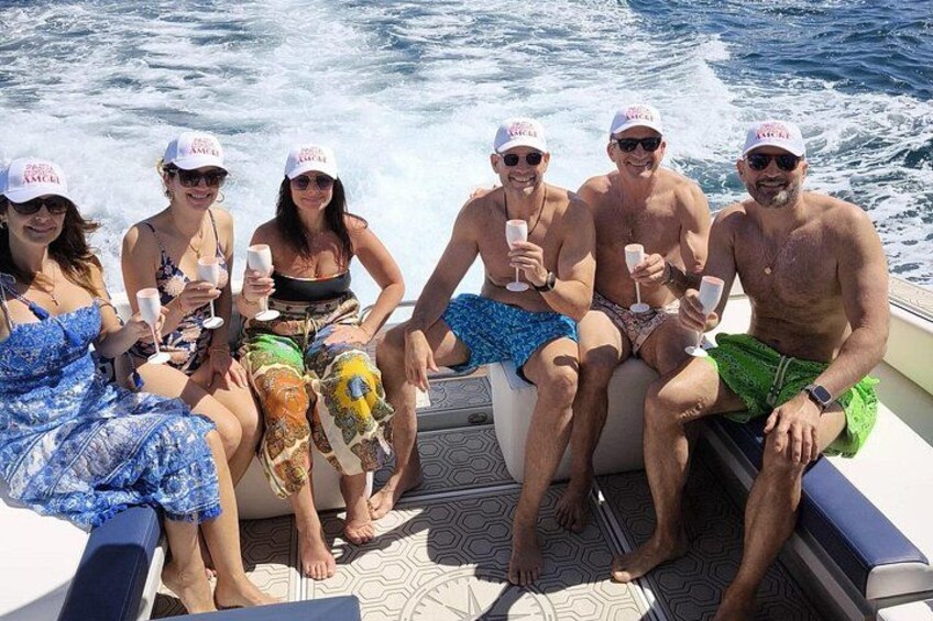 Un grupo de personas en un bote, sosteniendo bebidas, con agua de fondo. 5