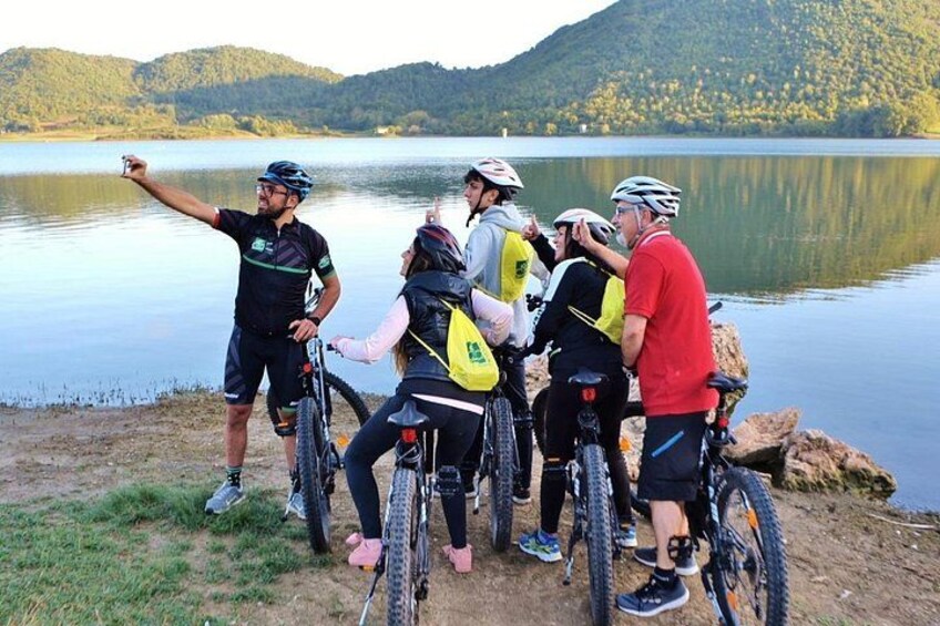 A group of cyclists by a lake with mountains in the background. 1