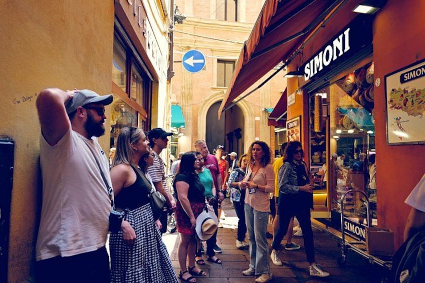A street with people standing and walking, a SIMONI store, and a blue directional sign. 5