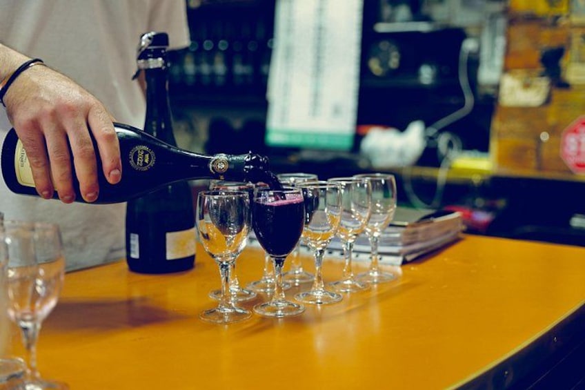 A person pouring a dark liquid from a bottle into several glasses on a bar counter. 4