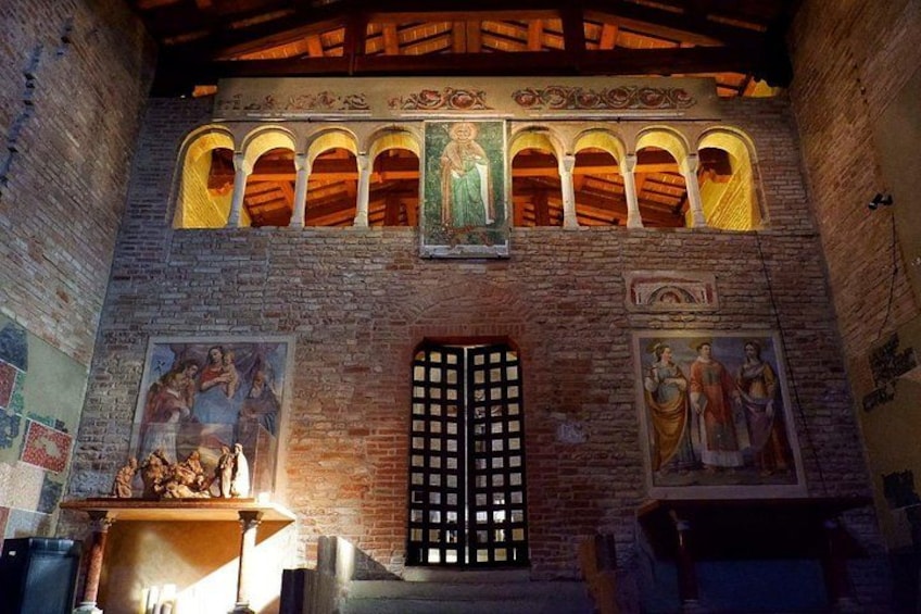 A church interior with arched windows, a central door, and frescoes on the walls. 1