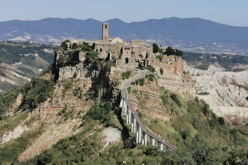A historic castle on a cliff with a watchtower, surrounded by rugged terrain and a bridge. 1