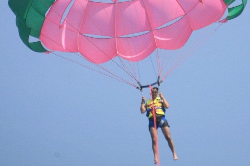 En person paraglider med en pink og grøn faldskærm mod en klar blå himmel. 2