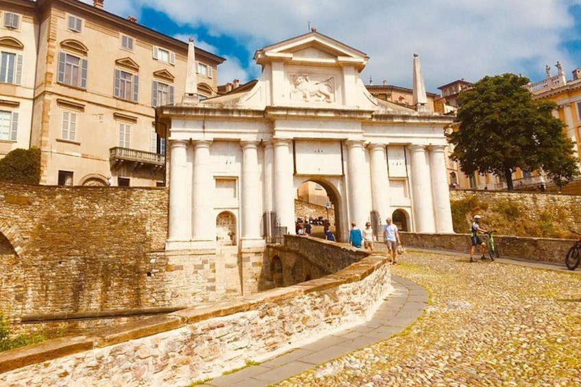 Un arco histórico con arquitectura clásica, un camino empedrado y un muro de piedra. 4