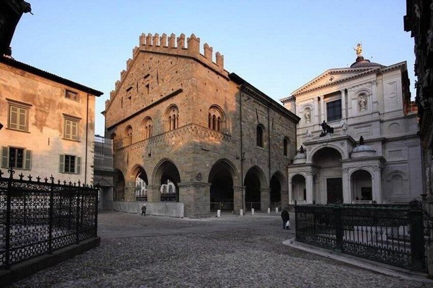 A historical building with arches and a tower, surrounded by cobblestone streets and other old buildings. 3