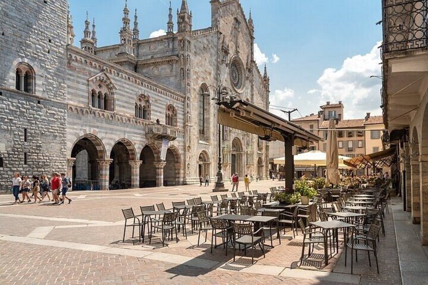 A historic plaza with stone buildings, outdoor seating, and people walking. 4