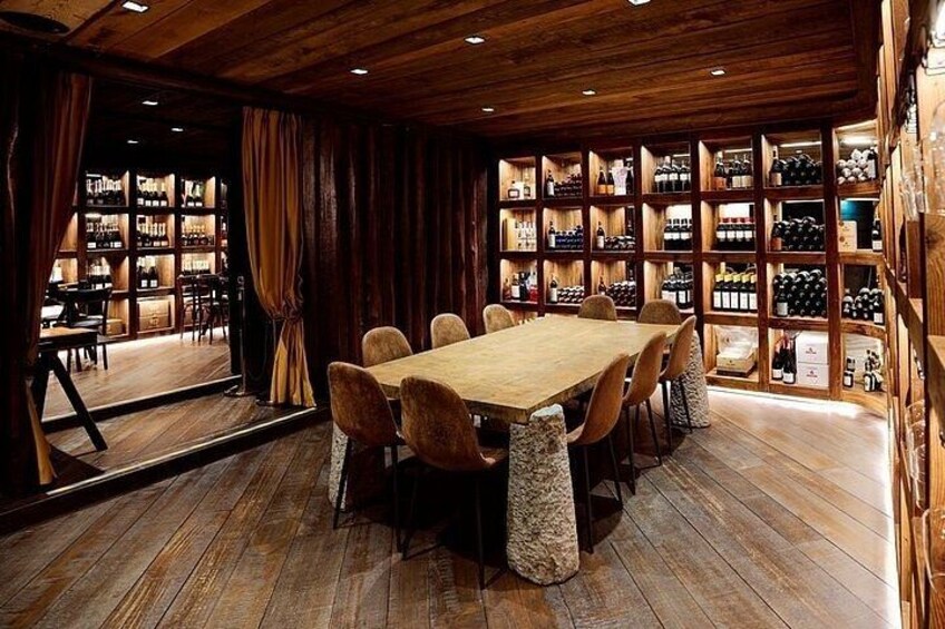 A wooden-paneled room with a large table and chairs, surrounded by shelves of wine bottles. 3