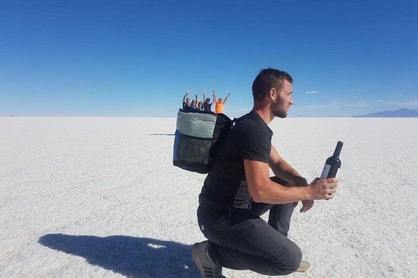 A person kneeling on a vast white salt flat with a backpack and a bottle. 2
