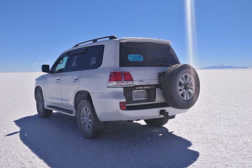 A white SUV parked on a vast salt flat with a clear sky. 4
