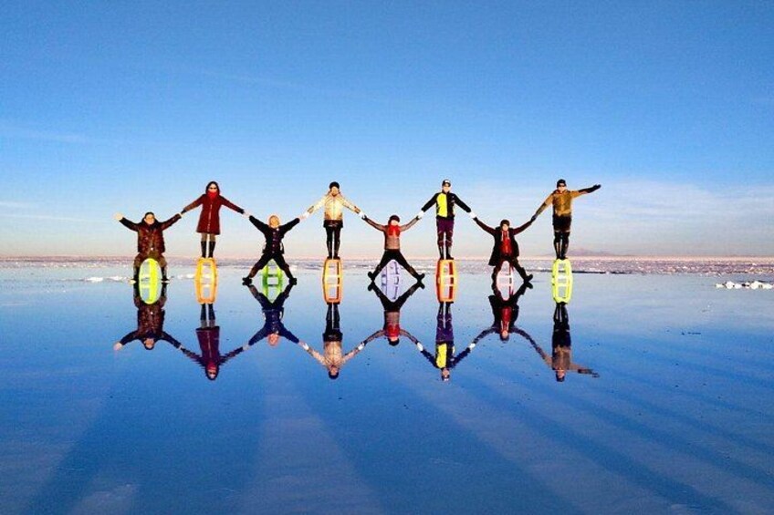 A group of people standing on a reflective surface with their arms outstretched, creating a symmetrical reflection. 3