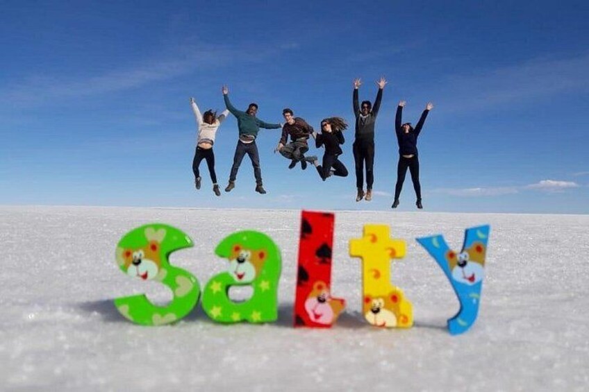 Mensen springen in de lucht boven kleurrijke letters die 'SALTY' vormen op een besneeuwde ondergrond. 1