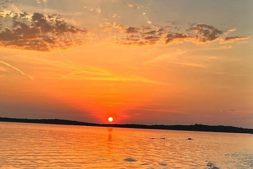 A sunset over a calm body of water with a silhouette of land in the distance. 2