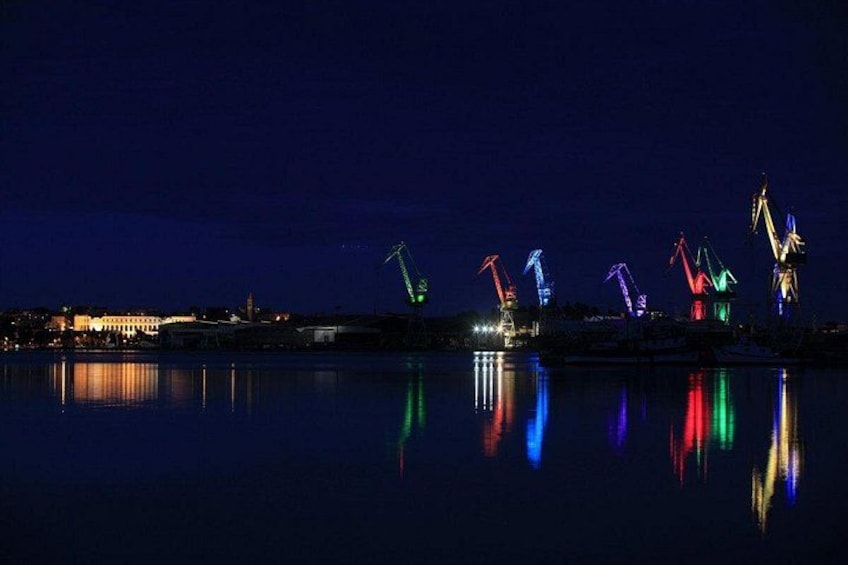 A nighttime view of a waterfront with illuminated cranes and buildings reflecting on the water. 5