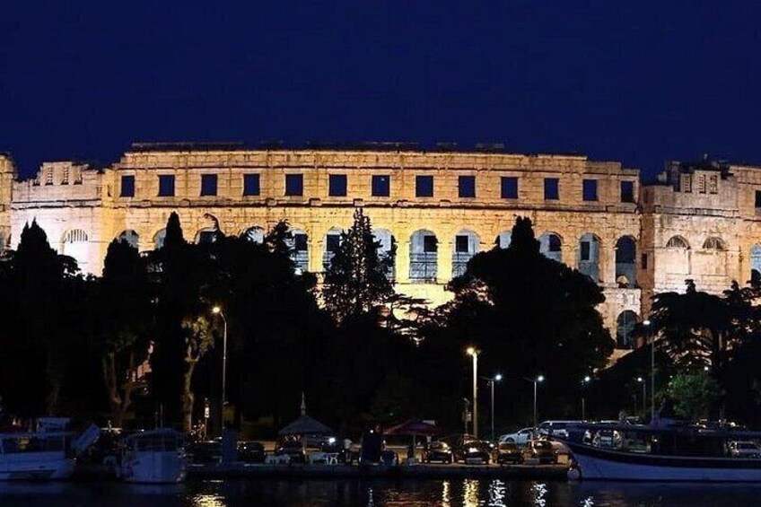 A historic building with arches and columns, illuminated at night, with trees and a body of water in the foreground. 4