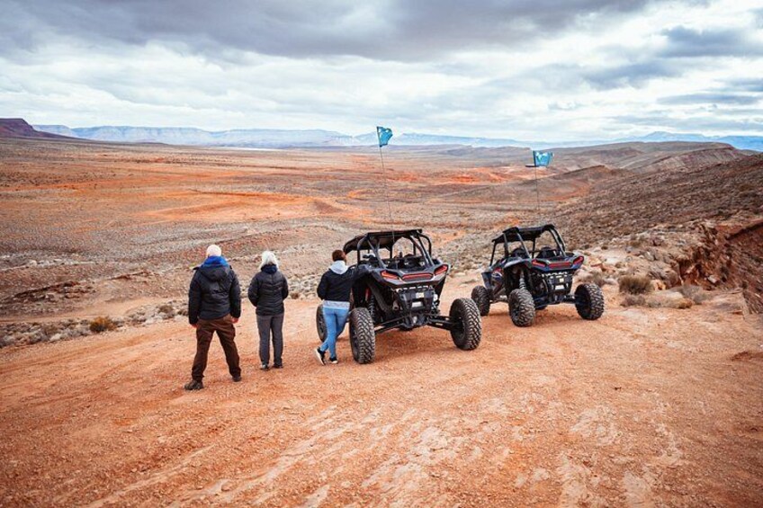A group of people standing on a dirt road with off-road vehicles in a barren landscape. 2