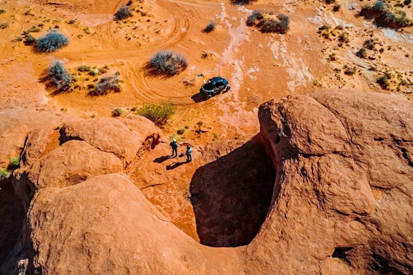 A desert landscape with red rock formations, a large hole, and a vehicle. 4
