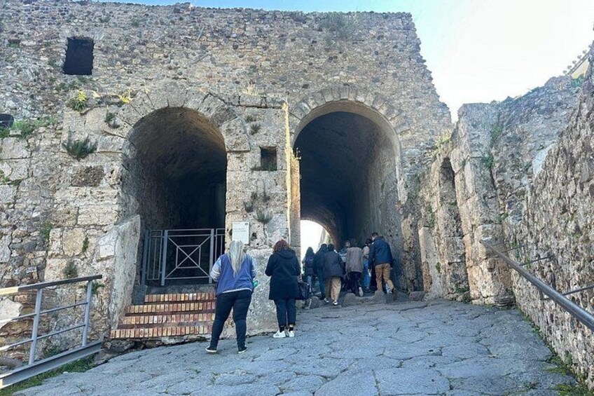 A stone archway leading into a tunnel, with people walking through it. 2