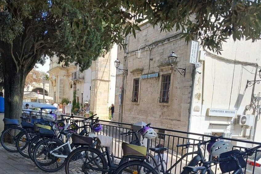 A tree-lined street with parked bicycles, a building with a sign reading 'COPISTEIA RECIBIDA,' and a parked blue vehicle. 2