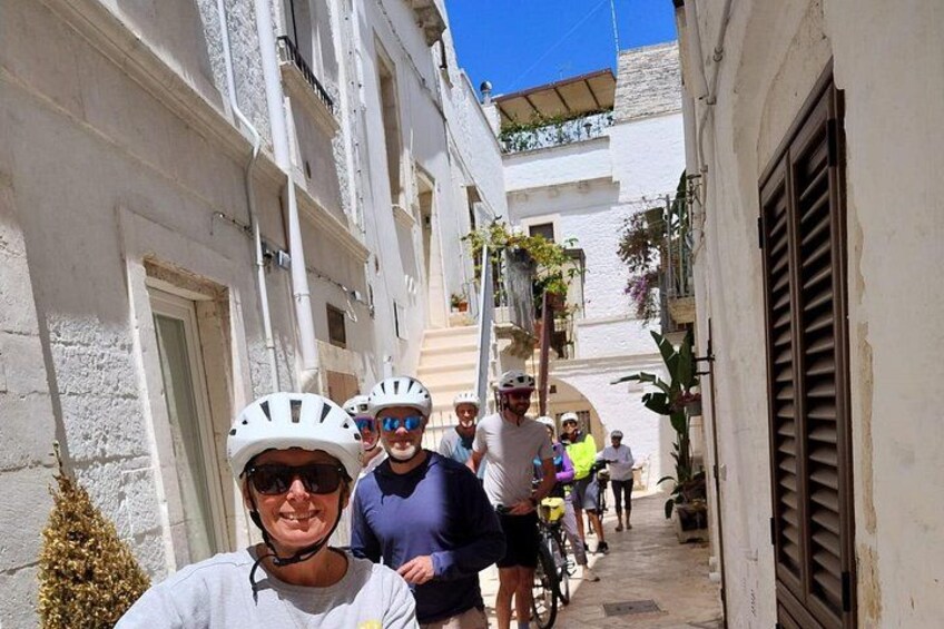 A group of cyclists on a narrow street with white buildings and balconies. 1