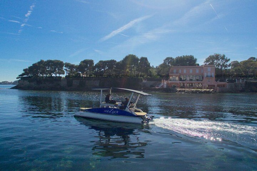 A speedboat on calm water, a red building on a cliff, and trees in the background. 3