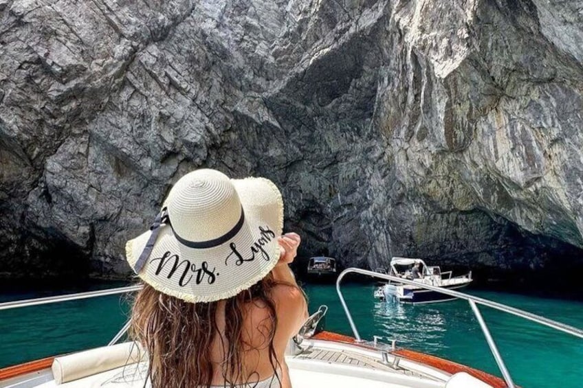 A boat with a person wearing a hat with 'Mrs. Lyons' on it, a rocky cliff, and another boat in the background. 3