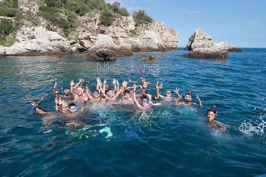 A group of people swimming in clear blue water with rocky cliffs in the background. 1