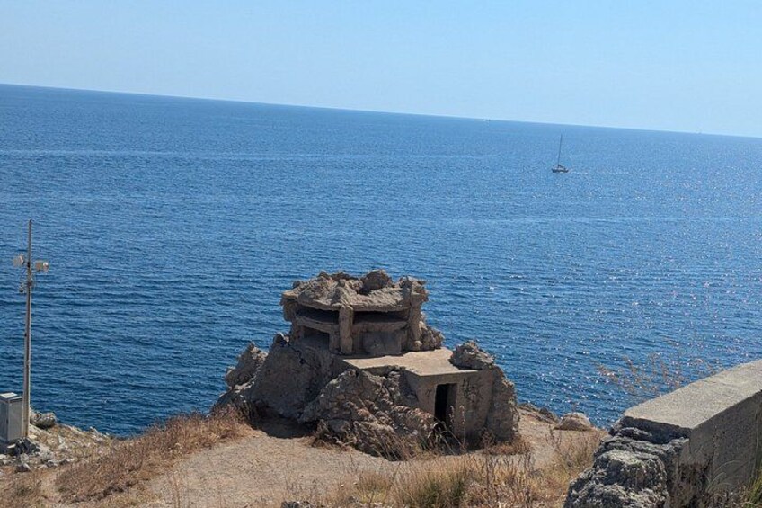 A coastal landscape with a rocky structure and a clear blue sea. 4