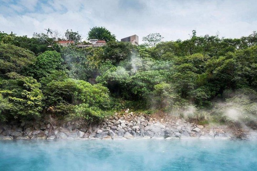 A hot spring surrounded by lush greenery and a rocky shoreline. 1