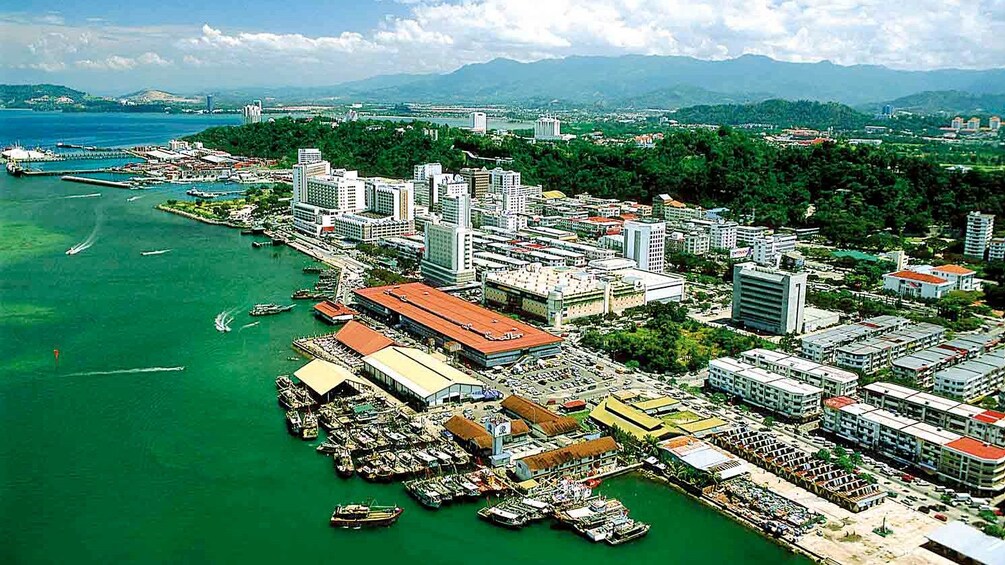 An aerial view of a coastal city with dense urban development, a marina, and a mountainous backdrop. 3
