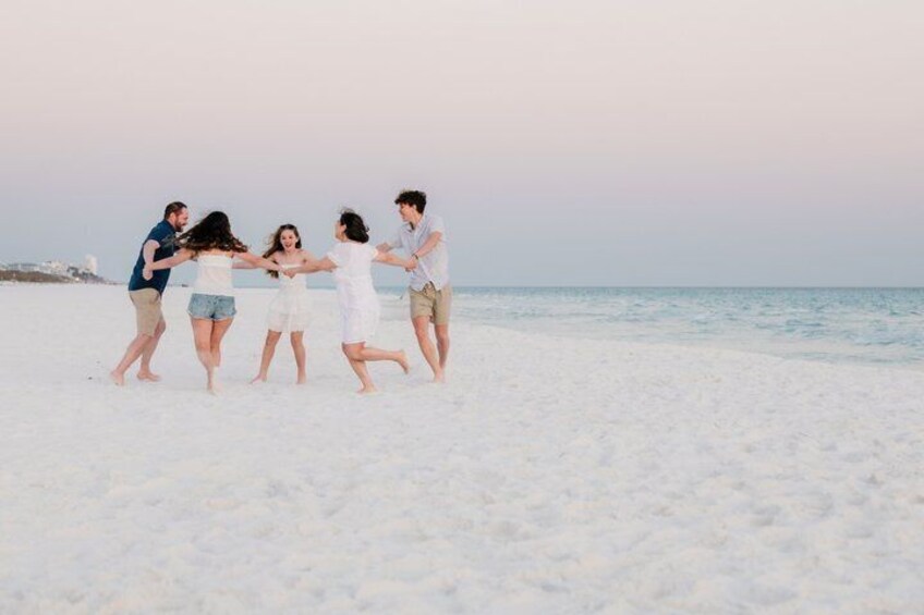A group of people holding hands on a sandy beach with the ocean in the background. 5