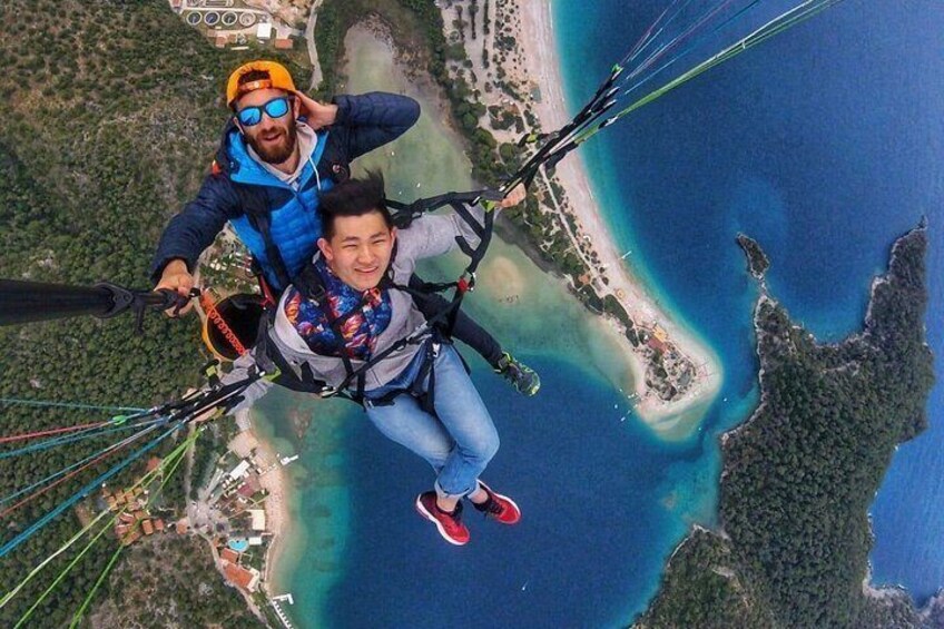 Two people paragliding over a coastal area with clear blue waters and a beach. 2