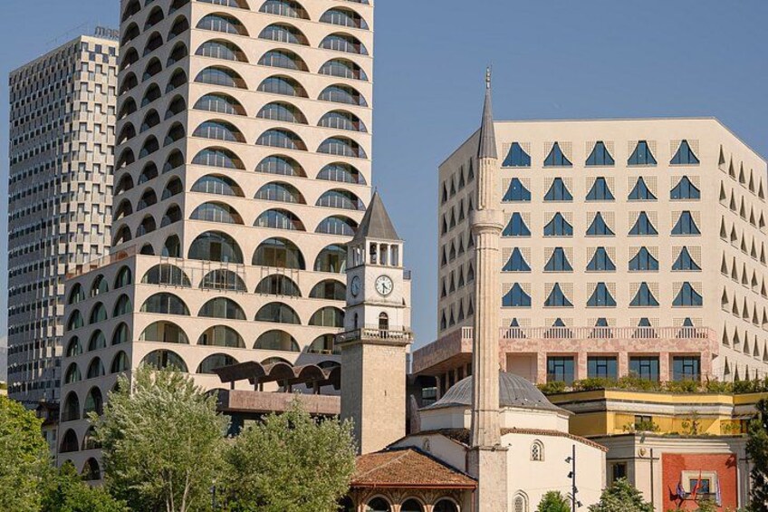 Un paysage urbain avec des bâtiments modernes, dont un beffroi et un immeuble doté d’une façade ornée d’une série de fenêtres triangulaires originales. 2