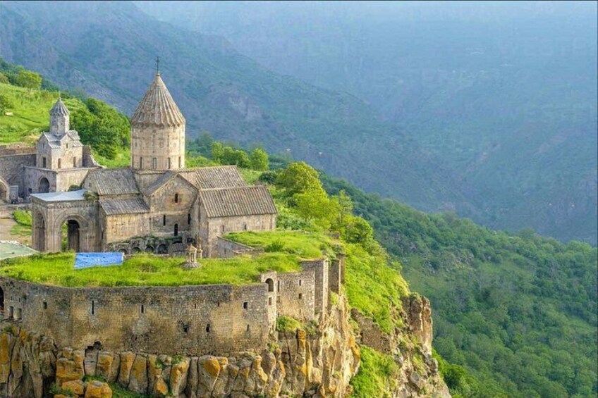 A historic church on a cliffside with a mountainous backdrop. 1