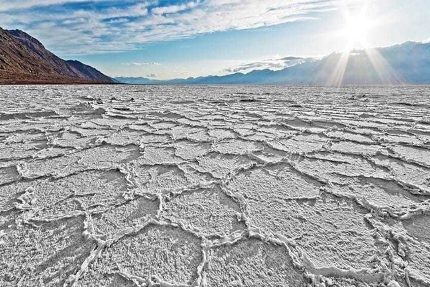 Una vasta distesa salata con terreno screpolato e montagne lontane sotto un cielo sereno. 2