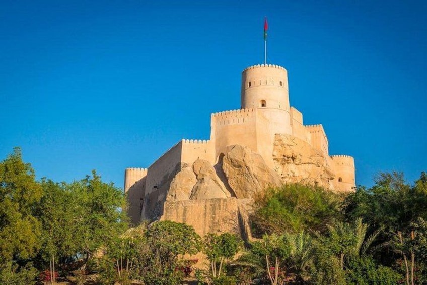 A large fortress-like structure with a prominent round tower, set against a clear blue sky. 3