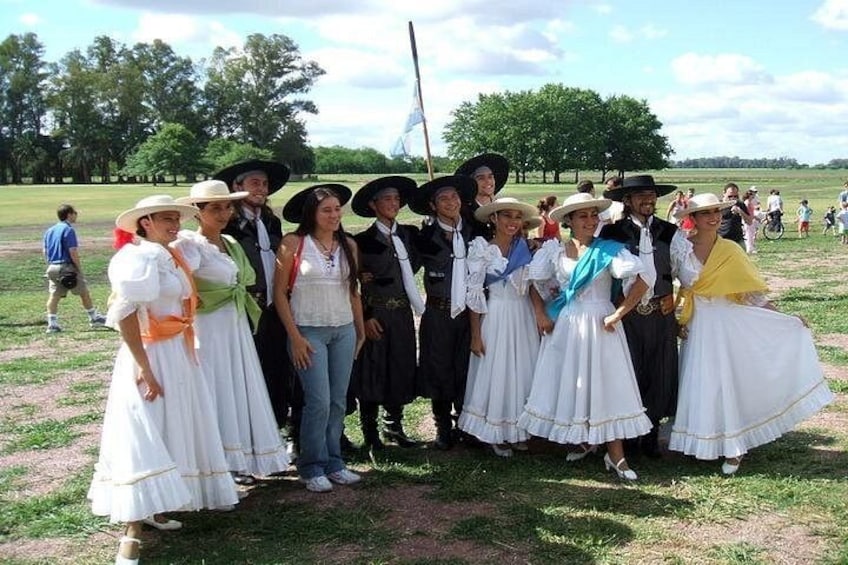 A group of people in traditional European attire posing for a photo in an outdoor setting with trees and grass. 4