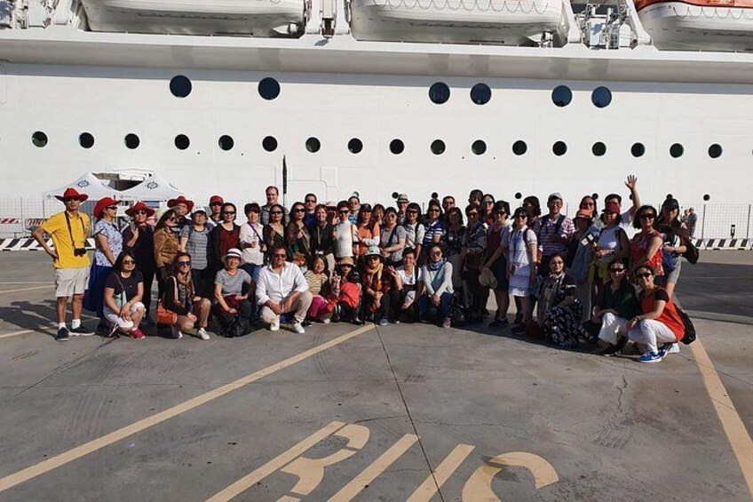 Eine Gruppe von Menschen posiert vor einem großen Kreuzfahrtschiff. 1