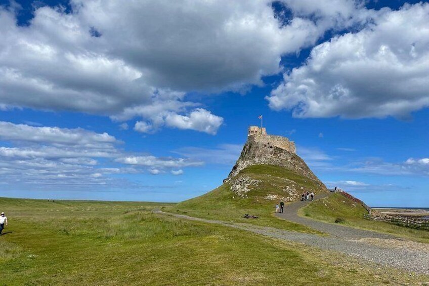 A grassy hill with a stone structure on top, a clear sky, and a few people walking on a path. 2