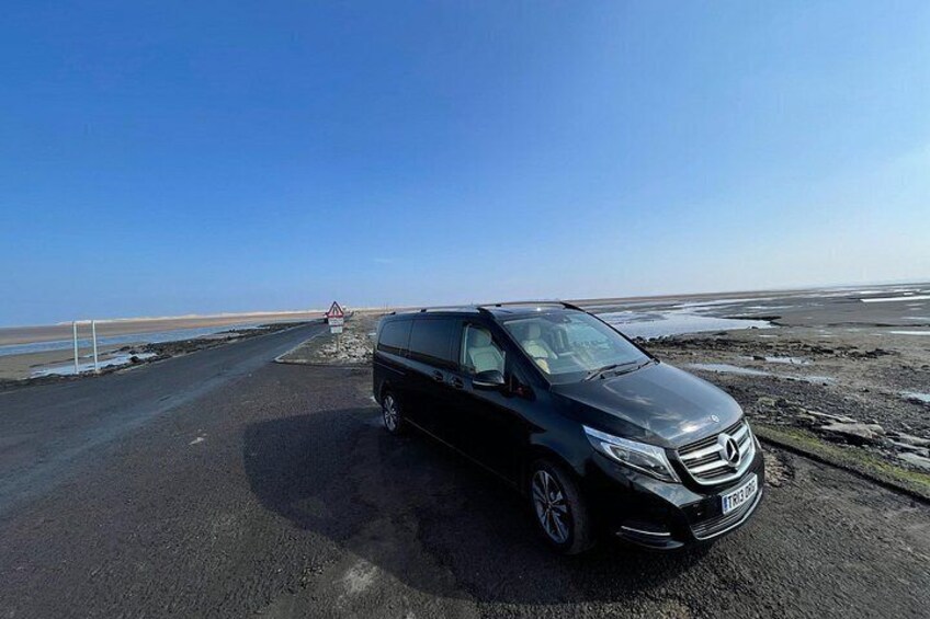 A black car parked on a road with a warning sign in the distance. 4