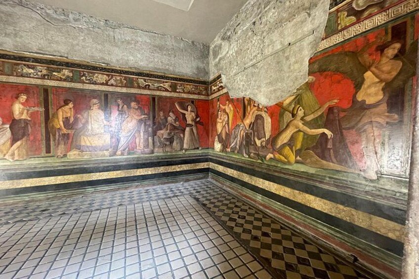 A mosaic with figures in red and gold, a checkered floor, and a stone wall. 2