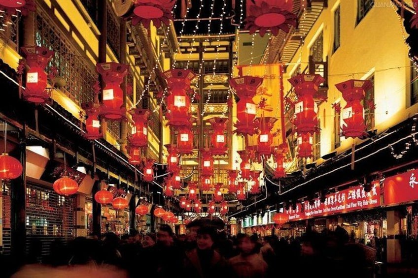 A street lined with traditional buildings, adorned with red lanterns and illuminated signs. 1